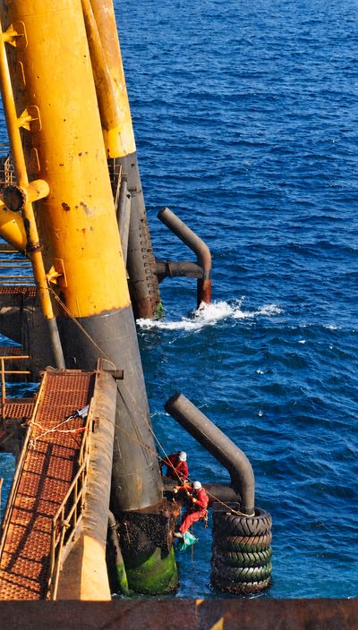Two rope access technicians working down a platform leg above open water.