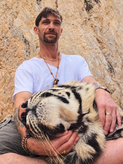 Jimi Gill sitting with a sleeping tiger resting against him.